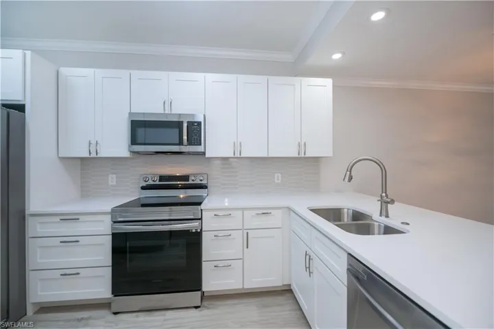 Kitchen featuring appliances with stainless steel finishes, ornamental molding, white cabinetry, light stone counters, and decorative backsplash