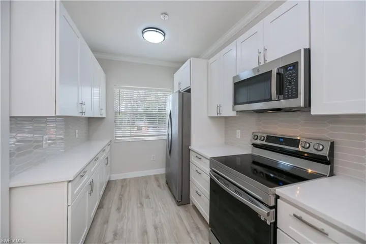 Kitchen with tasteful backsplash, appliances with stainless steel finishes, white cabinetry, ornamental molding, and light wood finished floors