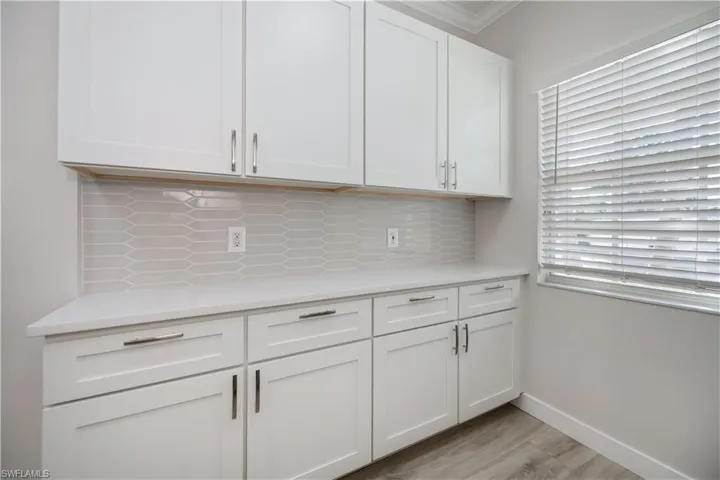 Kitchen featuring white cabinets, tasteful backsplash, light wood-style flooring, light stone counters, and ornamental molding