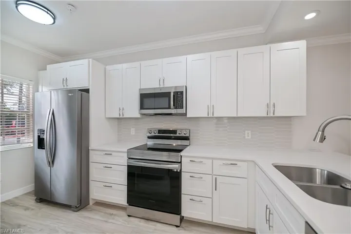Kitchen with crown molding, appliances with stainless steel finishes, white cabinetry, light stone counters, and backsplash