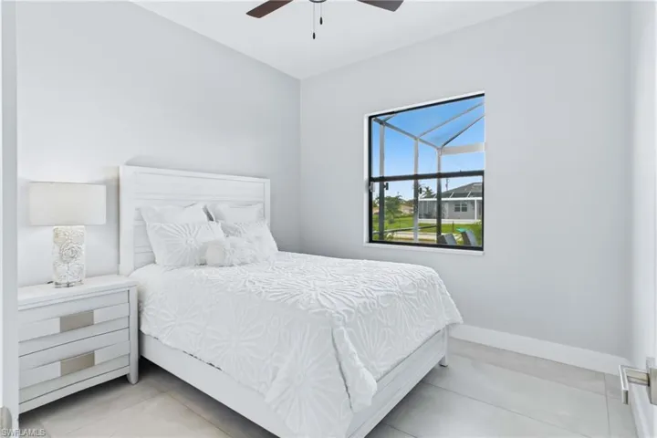 Bright room featuring a window overlooking an outdoor screened area, light-toned walls, tile flooring, and a ceiling fan