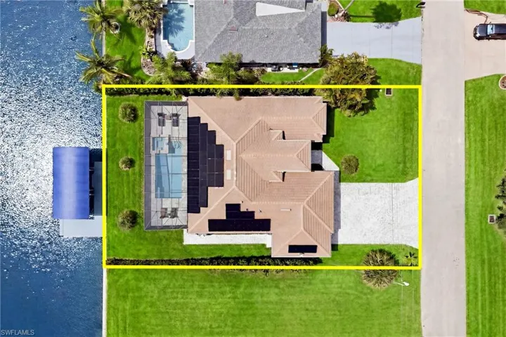 Waterfront property featuring a private boat dock, screened pool enclosure, tile roof, solar panels, and a concrete driveway