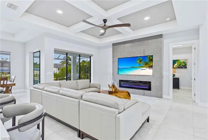 Expansive living area featuring a modern media wall with an integrated electric fireplace, large format tile flooring, and a coffered ceiling with recessed lighting