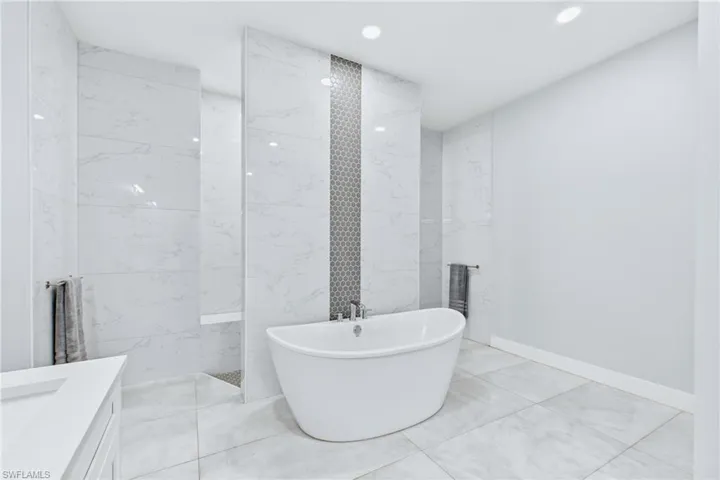 Freestanding soaking tub with a hexagon tile accent wall, large format floor tile, and a walk-in shower with a built-in bench