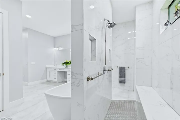 Spacious bathroom featuring a frameless glass shower with a built-in bench, marble-finish tile walls, and a recessed niche