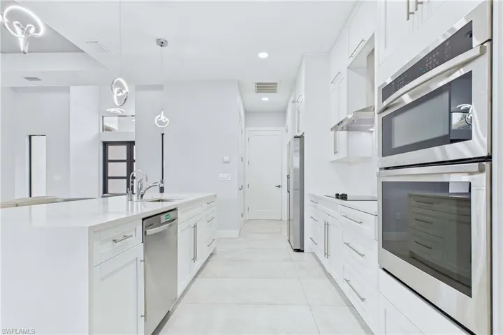 Bright kitchen featuring white cabinetry, stainless steel appliances, a center island with sink, pendant lighting, and tiled flooring