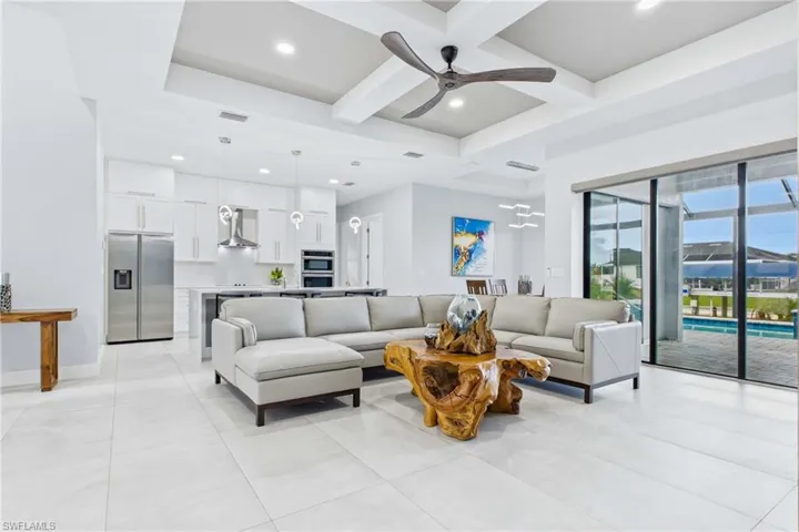 Open-concept living area featuring a tray ceiling with a modern ceiling fan, large format tile flooring, and sliding glass doors opening to an outdoor pool area