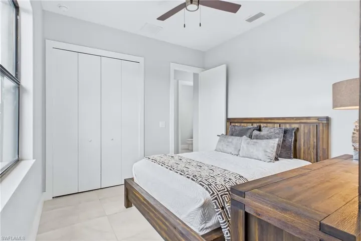 Bedroom featuring light tile flooring, a large window, bi-fold closet doors, and a ceiling fan