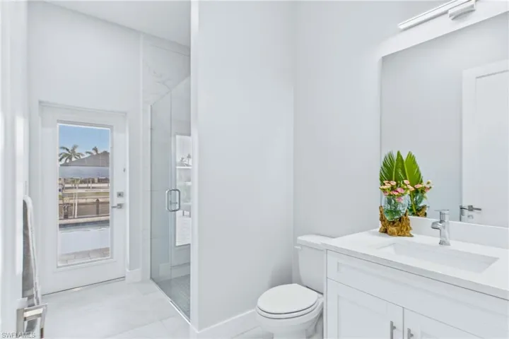 Bright bathroom featuring a glass-enclosed shower with tile surround, white vanity with integrated sink, and an exterior door providing water views