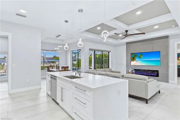 Open-concept living space featuring a large kitchen island with integrated sink, stainless steel dishwasher, and white cabinetry