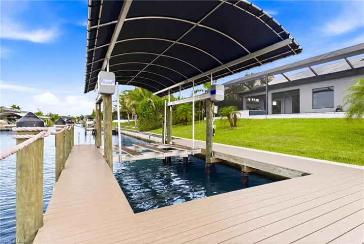 Waterfront dock featuring a covered boat lift, composite decking, and robust pilings with rope accents
