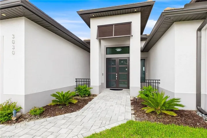 Contemporary exterior featuring a stepped entry with a paver walkway, double glass-paneled entry doors, and a decorative slatted transom