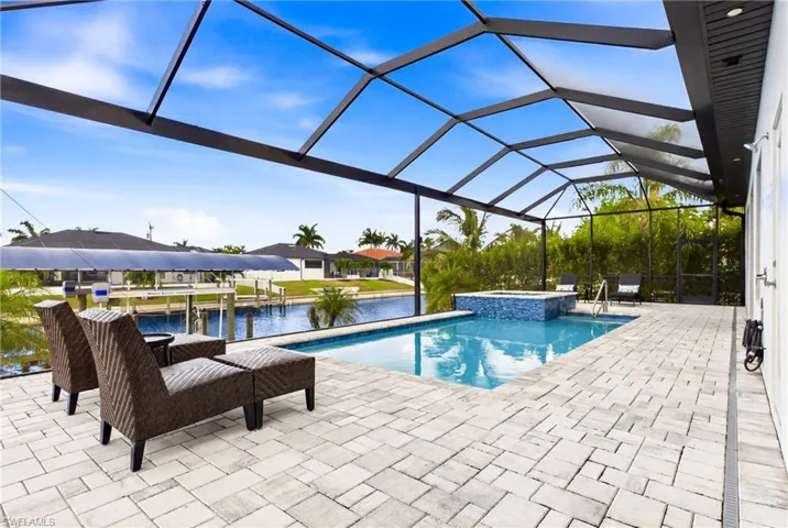 Screened outdoor living area featuring a rectangular pool, integrated spa with blue tile accents, and extensive paver patio