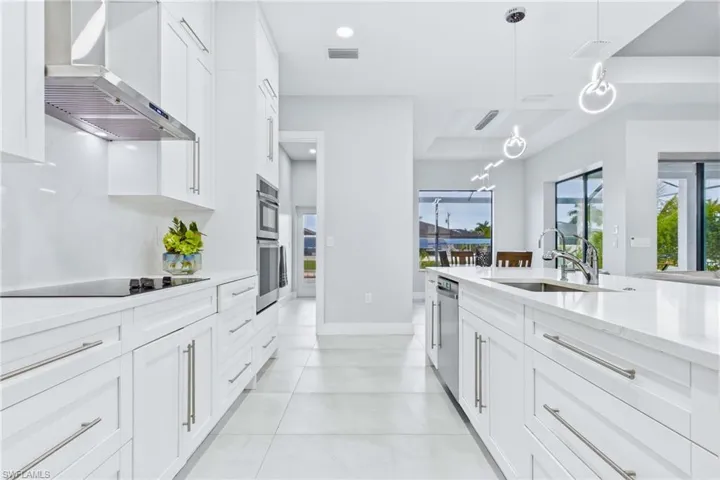 Modern kitchen with light-finish flooring, white cabinetry, integrated stainless steel appliances, and a central island featuring a sink and contemporary pendant lighting
