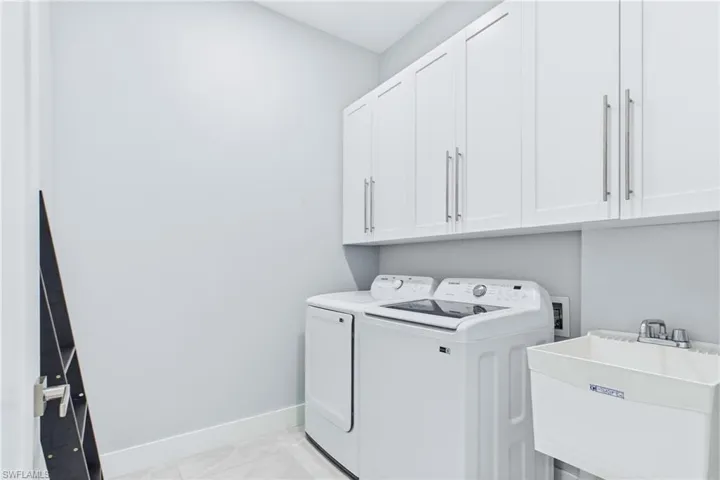 Laundry area featuring overhead white shaker cabinetry, a utility sink with dual-handle faucet, and light-toned tile flooring