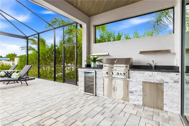 Screened outdoor living area featuring a built-in outdoor kitchen with a stainless steel grill, integrated wine refrigerator, and sink