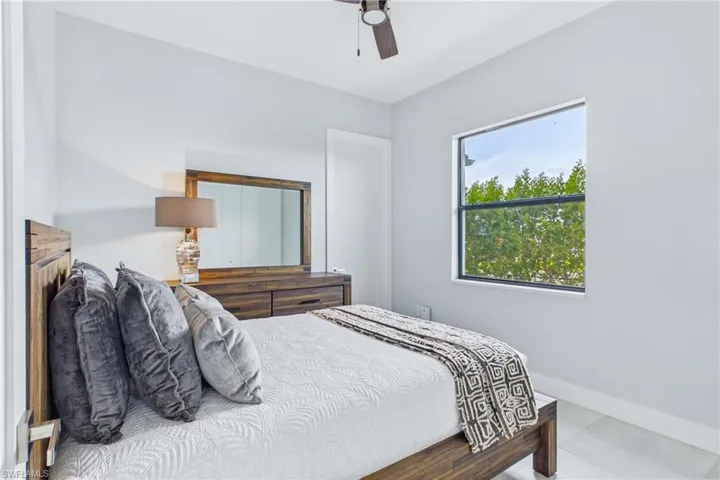 Bedroom featuring light gray walls, a ceiling fan, and a window with green tree foliage visible