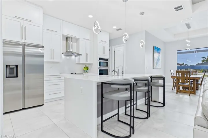 Modern kitchen featuring an expansive island with breakfast bar seating, stainless steel appliances, white cabinetry, and light tile flooring