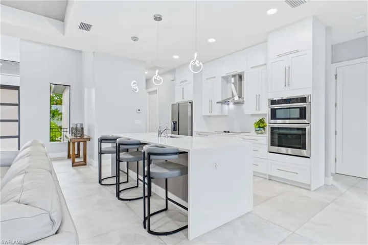 Modern kitchen featuring an expansive island with seating, white shaker-style cabinetry, stainless steel double ovens, and a contemporary range hood