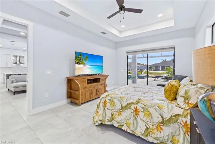 Spacious room featuring light-toned flooring, a tray ceiling with recessed lighting and a ceiling fan, and large sliding glass doors opening to an exterior screened patio with a pool