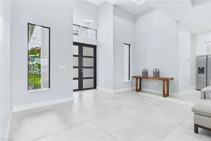 Entry foyer featuring double-height ceilings, large format tile flooring, and a contemporary entry door with frosted glass panels
