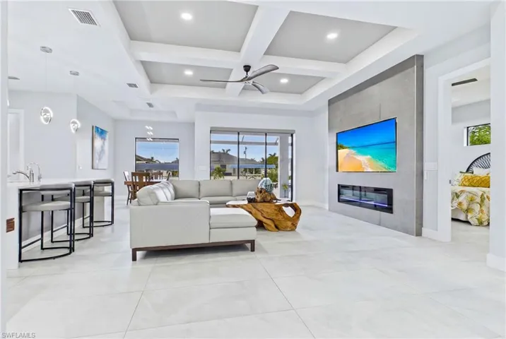 Open-concept living area featuring large format floor tiles, a coffered ceiling with recessed lighting and a ceiling fan, and sliding glass doors to the exterior