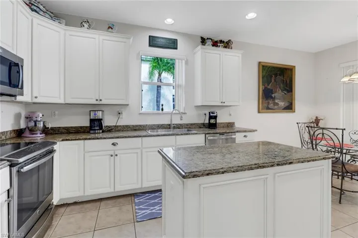 Kitchen featuring light tile patterned flooring, white cabinets, sink, appliances with stainless steel finishes, and a kitchen island