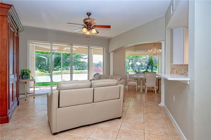 Living room featuring light tile patterned flooring, arched walkways, visible vents, and ceiling fan with notable chandelier