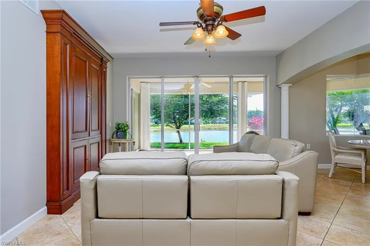 Living room with light tile patterned floors, arched walkways, ceiling fan, and baseboards