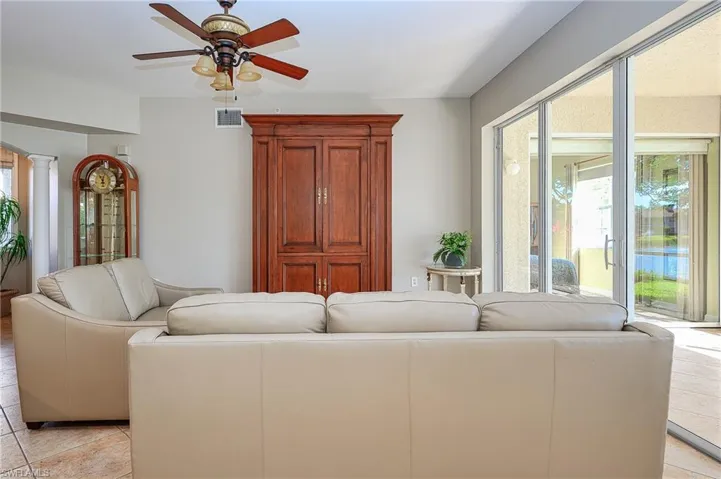 Living room with light tile patterned floors, visible vents, a ceiling fan, and decorative columns