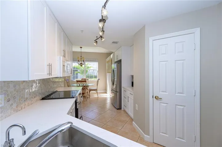 Kitchen featuring light stone countertops, decorative backsplash, stainless steel appliances, white cabinets, and light tile patterned flooring