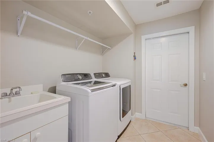 Laundry area with washing machine and clothes dryer, visible vents, baseboards, light tile patterned flooring, and cabinet space