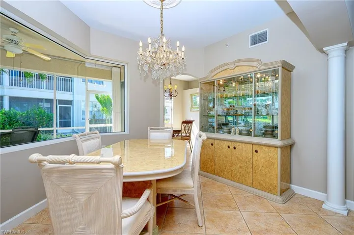 Dining room with decorative columns, light tile patterned floors, visible vents, and ceiling fan with notable chandelier