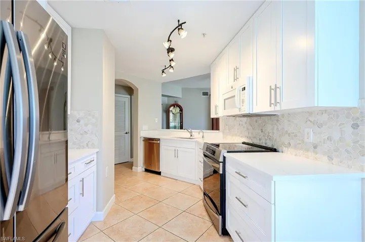 Kitchen featuring light tile patterned floors, a sink, stainless steel appliances, light countertops, and backsplash