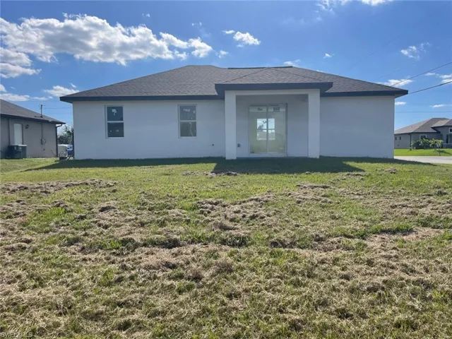 Rear view of property featuring stucco siding, central AC unit, a yard, and roof with shingles