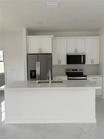 Kitchen with appliances with stainless steel finishes, light marble finish floors, an island with sink, white cabinets, and a sink