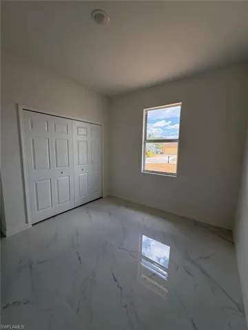 Unfurnished bedroom featuring light marble finish flooring, a closet, and baseboards