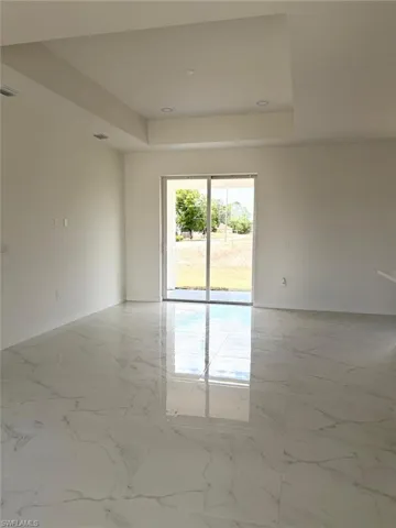 Unfurnished room featuring a tray ceiling, baseboards, and light marble finish flooring