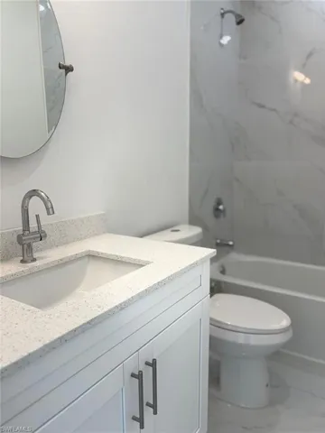 Full bath with vanity, toilet, marble look tiles, and shower / tub combination