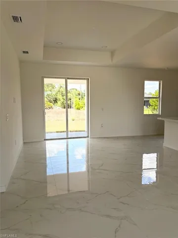 Empty room featuring a raised ceiling, baseboards, and light marble finish floors