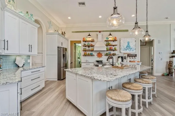 Kitchen featuring premium range hood, white cabinetry, hanging light fixtures, appliances with stainless steel finishes, and decorative backsplash