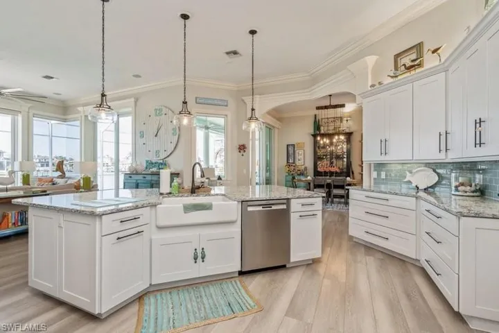 Kitchen with decorative light fixtures, light hardwood / wood-style flooring, stainless steel dishwasher, a kitchen island with sink, and white cabinets