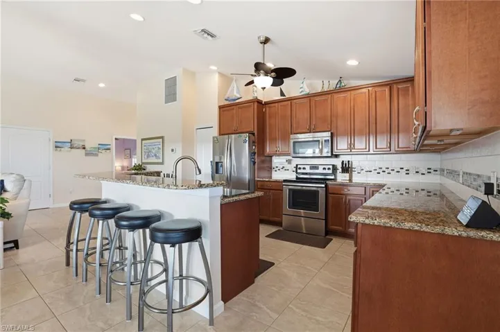 Kitchen featuring a breakfast bar, backsplash, stainless steel appliances, and a kitchen island with sink - Virtually Edited Image