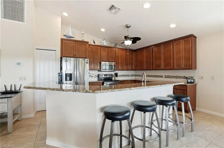 Kitchen featuring a breakfast bar, backsplash, stainless steel appliances, and a kitchen island with sink - Virtually Edited Image