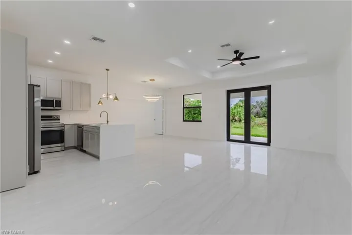 Kitchen with open floor plan, pendant lighting, gray cabinetry, a tray ceiling, and appliances with stainless steel finishes