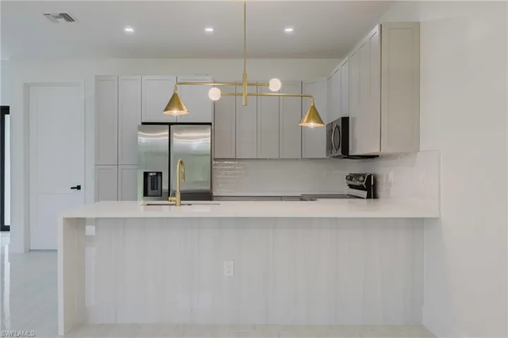 Kitchen featuring pendant lighting, stainless steel appliances, a peninsula, decorative backsplash, and light stone countertops