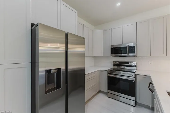 Kitchen featuring gray cabinets, stainless steel appliances, decorative backsplash, recessed lighting, and light stone countertops
