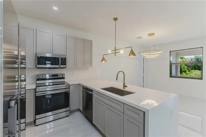Kitchen featuring gray cabinetry, stainless steel appliances, a peninsula, backsplash, and recessed lighting