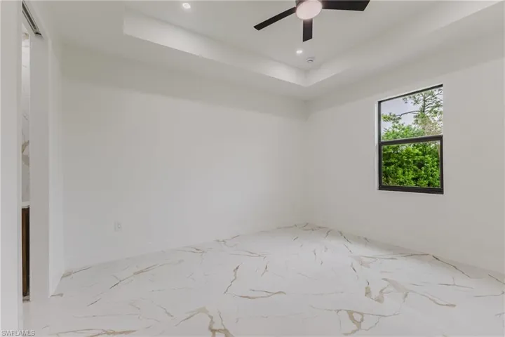 Empty room featuring a tray ceiling, recessed lighting, ceiling fan, and light marble finish flooring