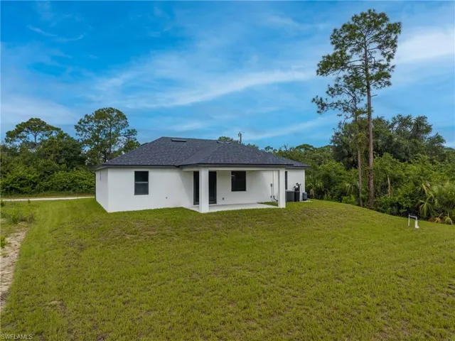 Back of property featuring a patio, stucco siding, a yard, and roof with shingles
